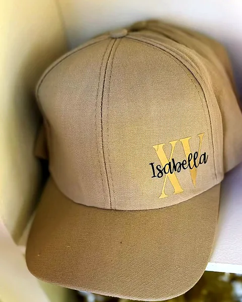 Tan baseball cap personalized with a gold XV monogram and the name Isabella in black script