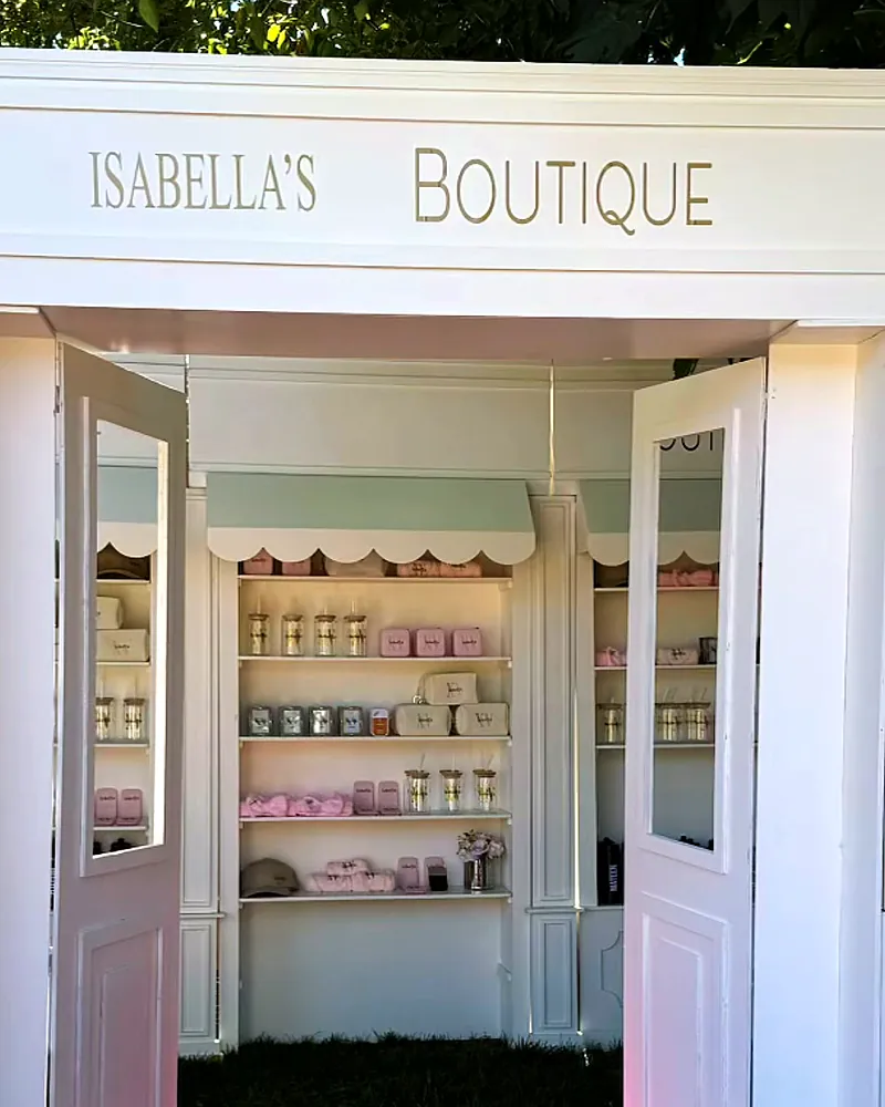 Boutique-style party favor display (shown here for a XV años celebration): white booth with open doors and pastel shelves of personalized caps, cups and pouches