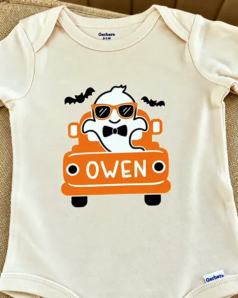 Cream baby onesie personalized with the name Owen on an orange truck carrying a ghost in sunglasses